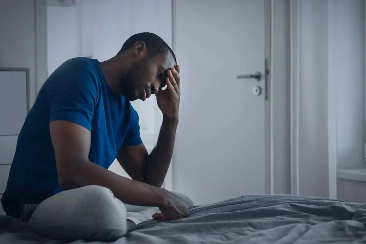 Man sitting on bed holding his head, reflecting after fentanyl detox